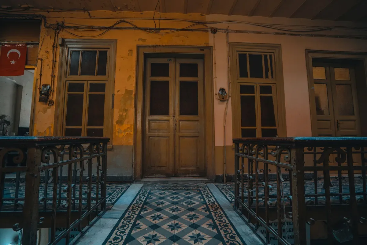 Street-level entrance with wooden double doors, patterned tiles, metal railings, and a red crescent-and-star flag.