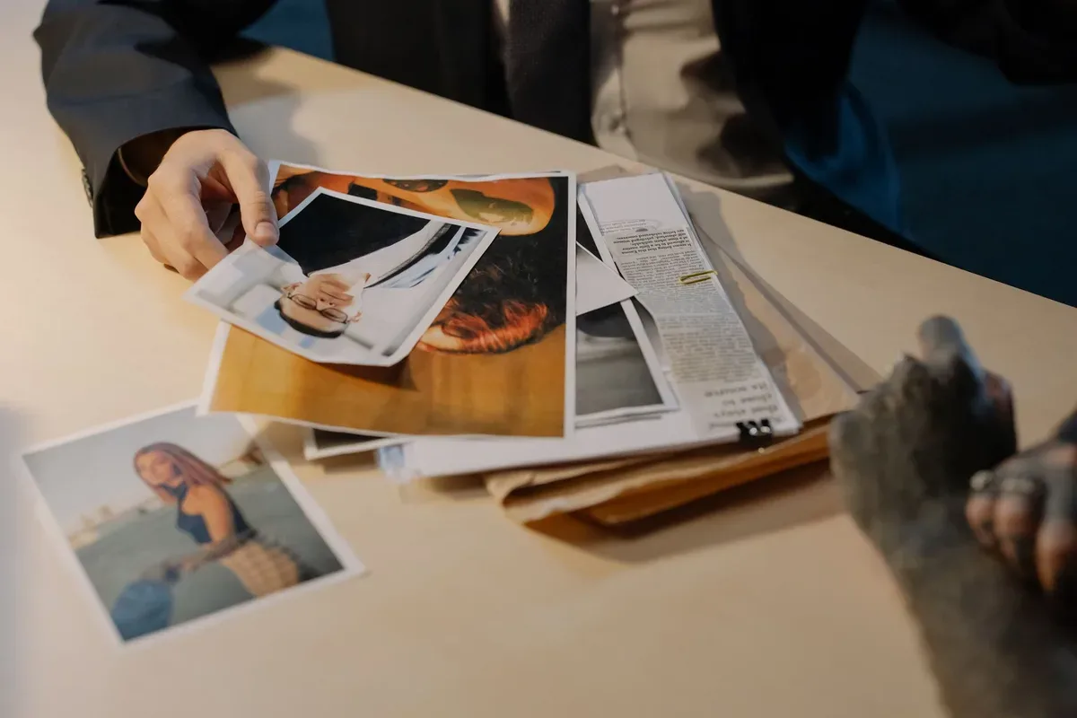 A person holds printed photographs over an open folder of papers on a table.