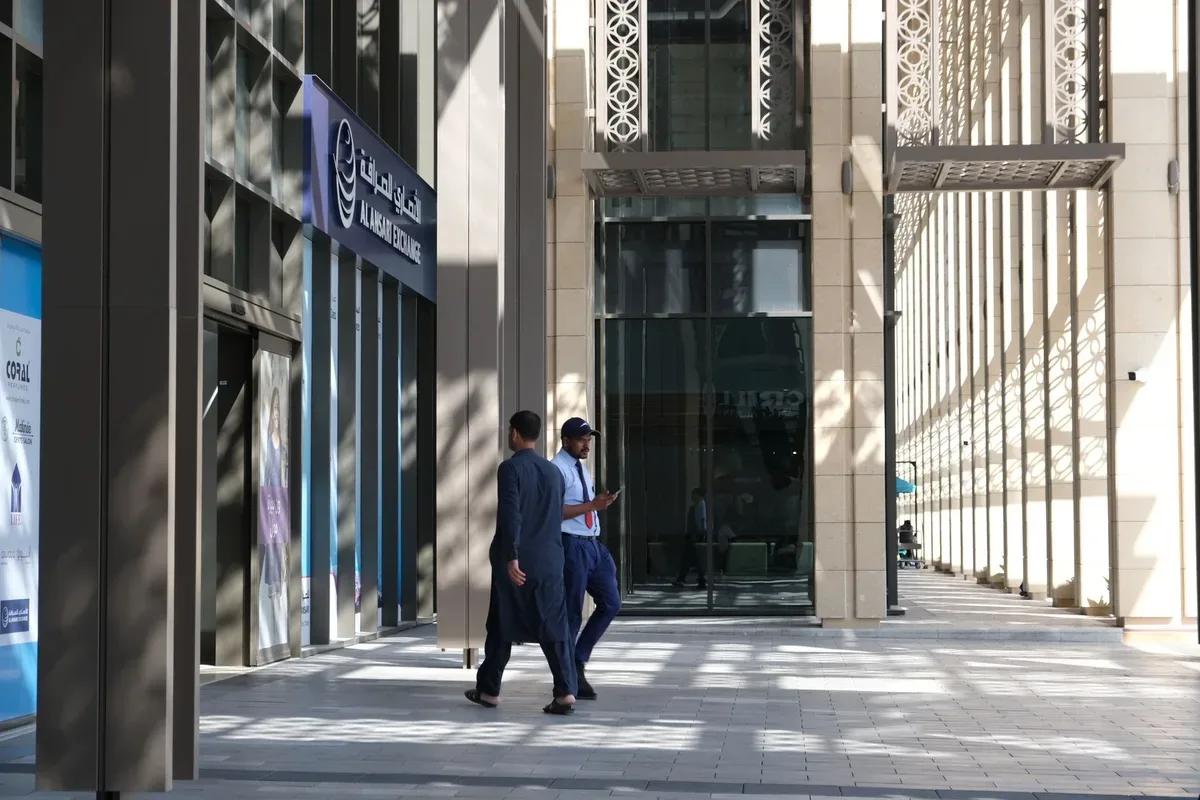 Two men in suits walking through the entrance of a modern glass and stone office building.